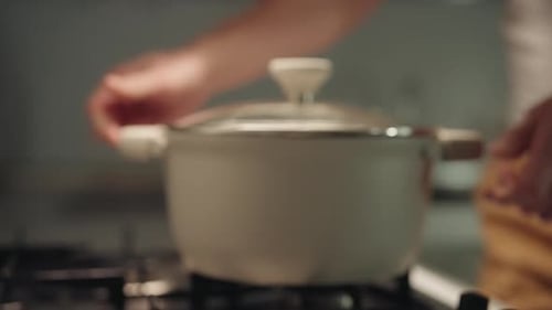 Selective Focus Shot of Man Placing Pot Onto Gas Stove and Turning Burner Preparing for Cooking