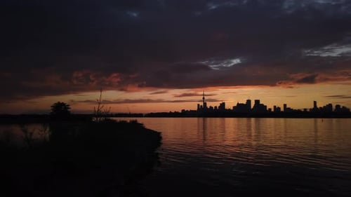 Dunkle Wolken rollen in einen wunderschönen Sonnenuntergang, mit einer Silhouette der Skyline von Toronto vor dem Horizont,