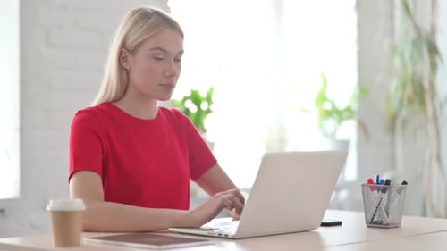 Young Blonde Woman Looking at Camera while using Laptop in Office