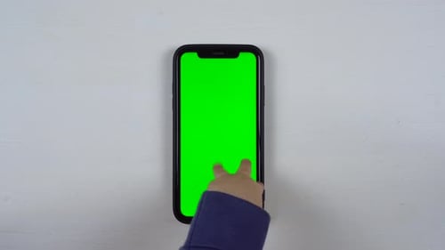 Infant Hand Interacting with Smartphone Green Screen on Table