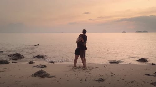 On Beach at Orange Sunset Loving Couple Embraces Surrounded By Romance of Orange Sky Romance of