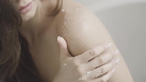 Woman applies exfoliating scrub to shoulder in close up