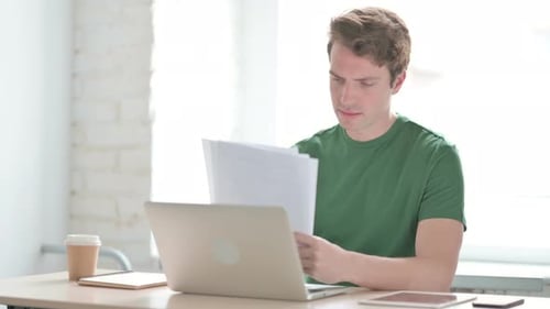 Man Reviews Documents While Working at Desk
