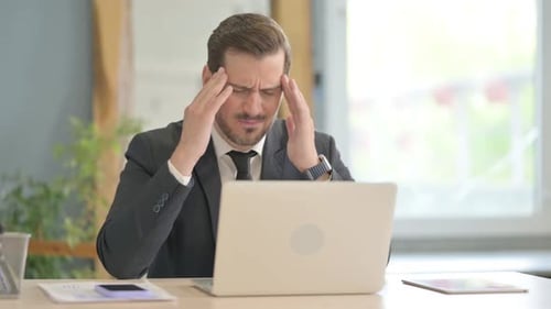 Tired Man Rubbing Temples and Eyes at Office Desk