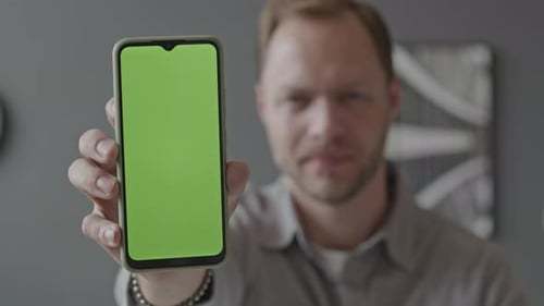 Man Demonstrating Smartphone with Green Screen at Camera