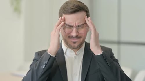 Stressed Young Man with a Headache in Office