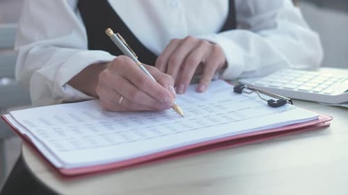Woman Writing on Financial Documents at Office Desk