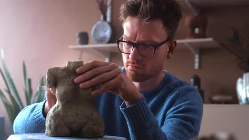 A Bearded Male Sculptor with Glasses Makes a Statue of a Female Figure A Ceramist Man Sculpts a