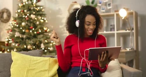 Chica africana en ropa casual en un hermoso apartamento decorado cerca de un fascinante árbol de Navidad y