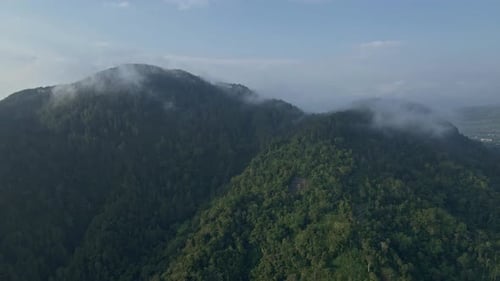 Sliding drone shot of rainforest-covered mountains. The fog that was starting to bend its peak. 4K a