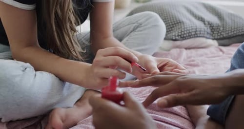Diverse teenage female friends sitting on bed and painting each other's fingernails
