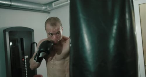 Concentrated man boxer punching boxing bag in gym. Slow motion and close up of male athlete at punch