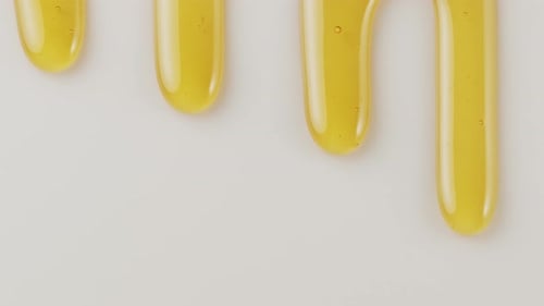 Drops of honey slowly flow down the white surface.