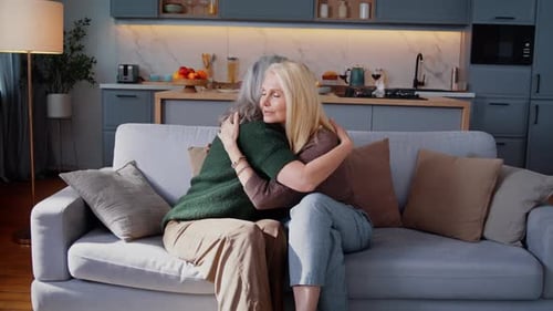 Elderly Women Hug Talking with Joyful Smiles on Sofa at Home