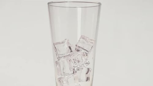 Ice Cubes Falls Into Clear Glass In White Background. - close up