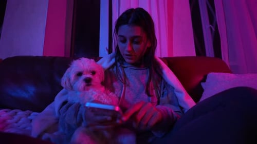 Young Woman Relaxes with Dog, Using Phone at Night