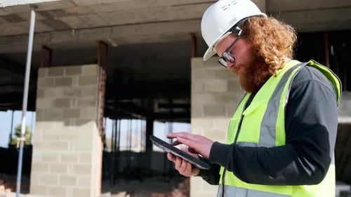 Construction worker using digital tablet on building site locking of screen, prepares a report