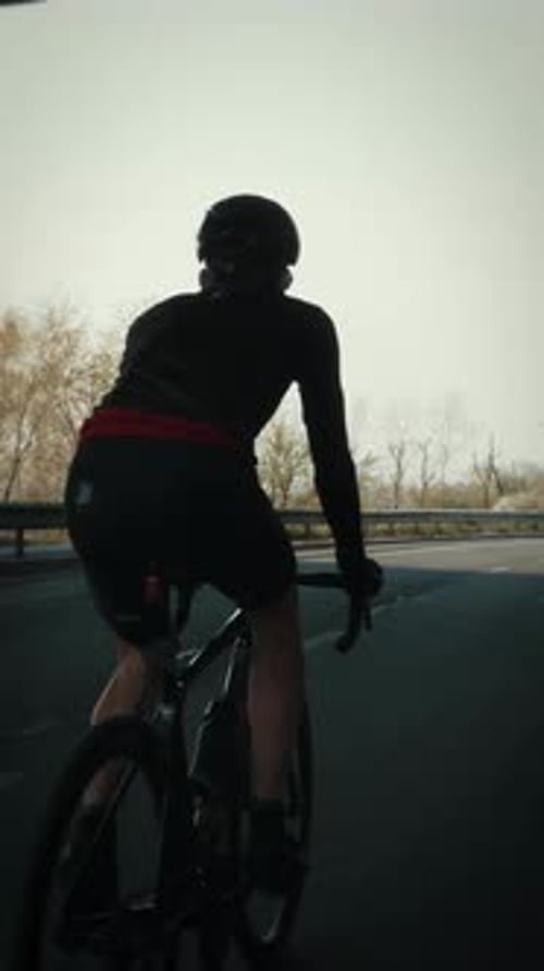 Man in cycling apparel riding bike on empty road under bridge. Vertical video