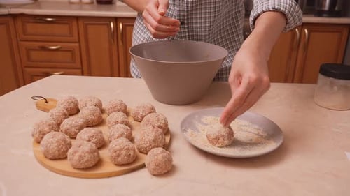 Woman Making Meatballs and Coating in Breadcrumbs in Kitchen