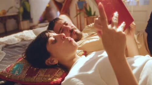 Couple Reading Book and Discussing It on Bed