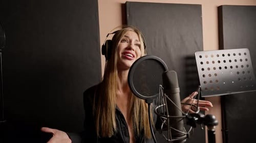 girl singer singing in a recording studio with headphones in front of microphone to create a song