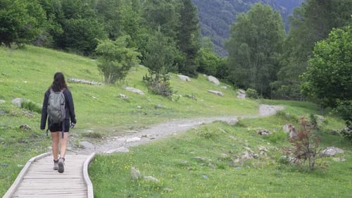 Girl trekking in nature with a backpack in a green mountainous environment on a trail