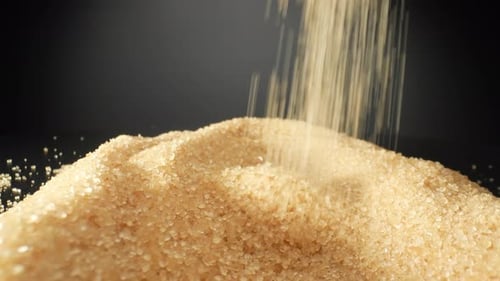 Golden brown sugar delicately cascading onto a sleek black background