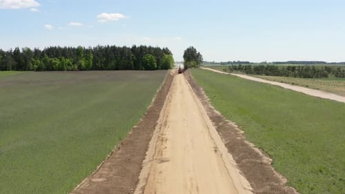 Bagger gräbt Straßenbett durch Ackerland und Wald. Straßenbau. Drohnenanflug