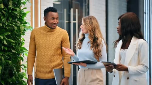 Multiracial group of workers walking in an office and discussing business affairs using tablets. Slo