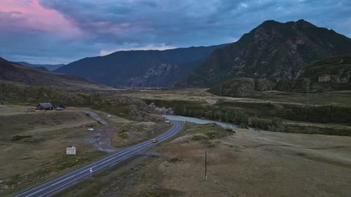 Luftbild eines Tals mit Fluss und Straße, umgeben von Bergen bei Sonnenuntergang