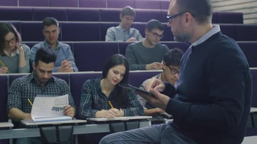 College professor is teaching a class of multi-ethnic students and checking a tablet computer.