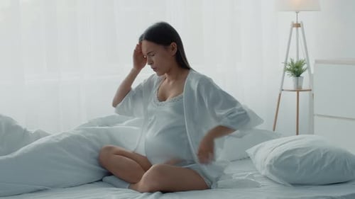 Pregnant Woman Experiencing Headache on Bed