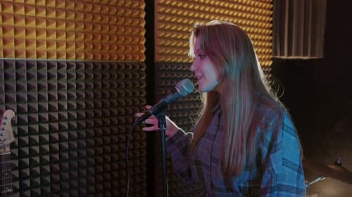 Young Pretty Woman with Long Hair Sings Into a Microphone in a Recording Studio