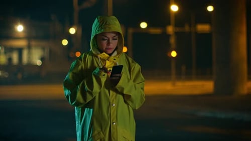 Woman in Raincoat Uses Mobile Phone at Night