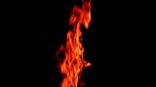Long and thin flame of the fire burning in the darkness isolated. Tiny sparkles rise up in the air.