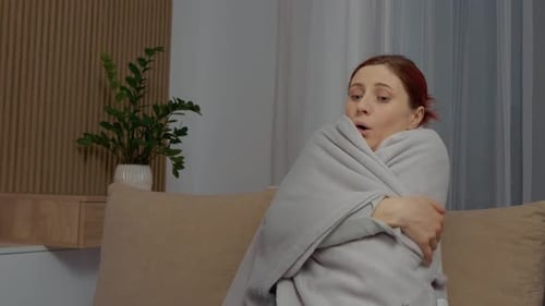 Une femme malade avec des frissons et des maux de gorge est assise sur le canapé en essayant de se rétablir