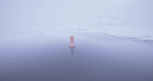 Bright Orange Buoy Stands Out in Foggy Waters Near Snowy Shore