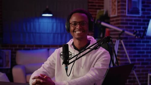 Portrait of African American Online Radio Host Sitting at Desk in Home Recording Studio with Boom