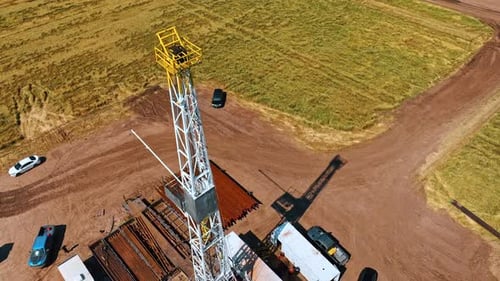 Footage around the top of the oil rig tower. Cars, metal pipes and people working on the location