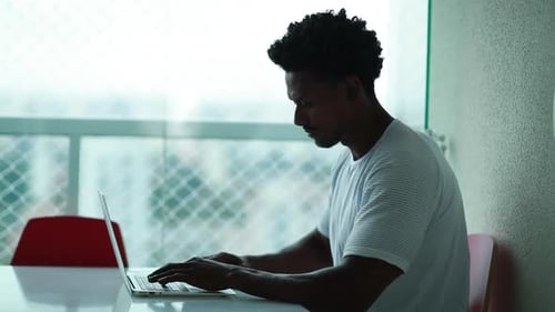Young Man Typing on Laptop at Table Indoors