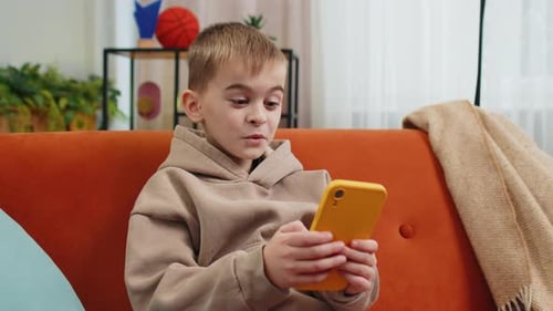 Boy Plays Phone Game on Orange Couch