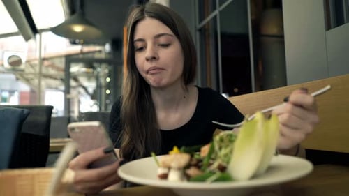 Young, Teenage Girl Texting On Smartphone And Eating Salad In Cafe