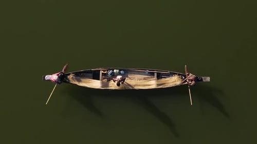 Aerial shot of a small wooden boat with fishermen catching fish using net in traditional style in Su