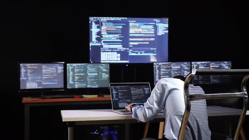 Programmeur s'appuyant sur une table tout en écrivant du code par un ordinateur portable utilisant plusieurs moniteurs affichant la base de données