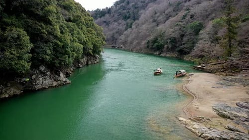 Filmmusik Drohnenaufnahme, die in Kyoto, Japan, einen Fluss hinunterfährt, vorbei an kleinen Booten