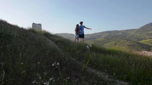 Couple looks out across rolling grass hills of Fez Morocco with wildflowers off path