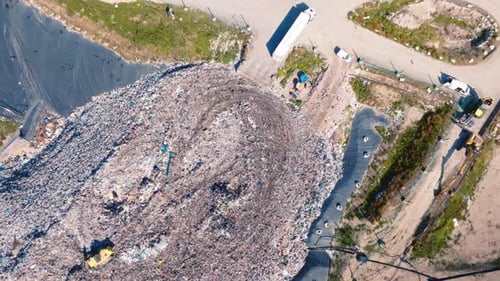 Very high drone shot above a mountain of garbage, a truck is pushing the garbage, there are lots of
