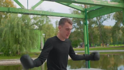 Male Fighter Training Vigorously Beneath Green Canopy By Water Male Martial Artist Engaging in