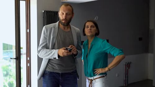 Young Couple Talking and Checking Project on Smartphone at New Home Analyzing