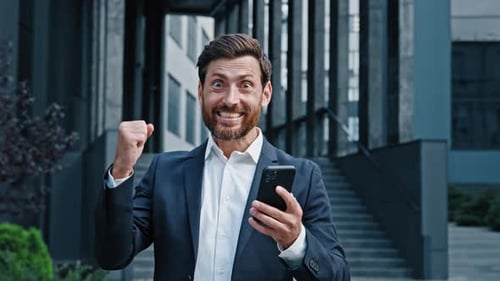 Excited Businessman Celebrating Success with Phone Outdoors